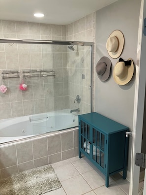 Une salle de bain avec une douche en verre, une baignoire, un meuble turquoise et trois chapeaux accrochés au mur.