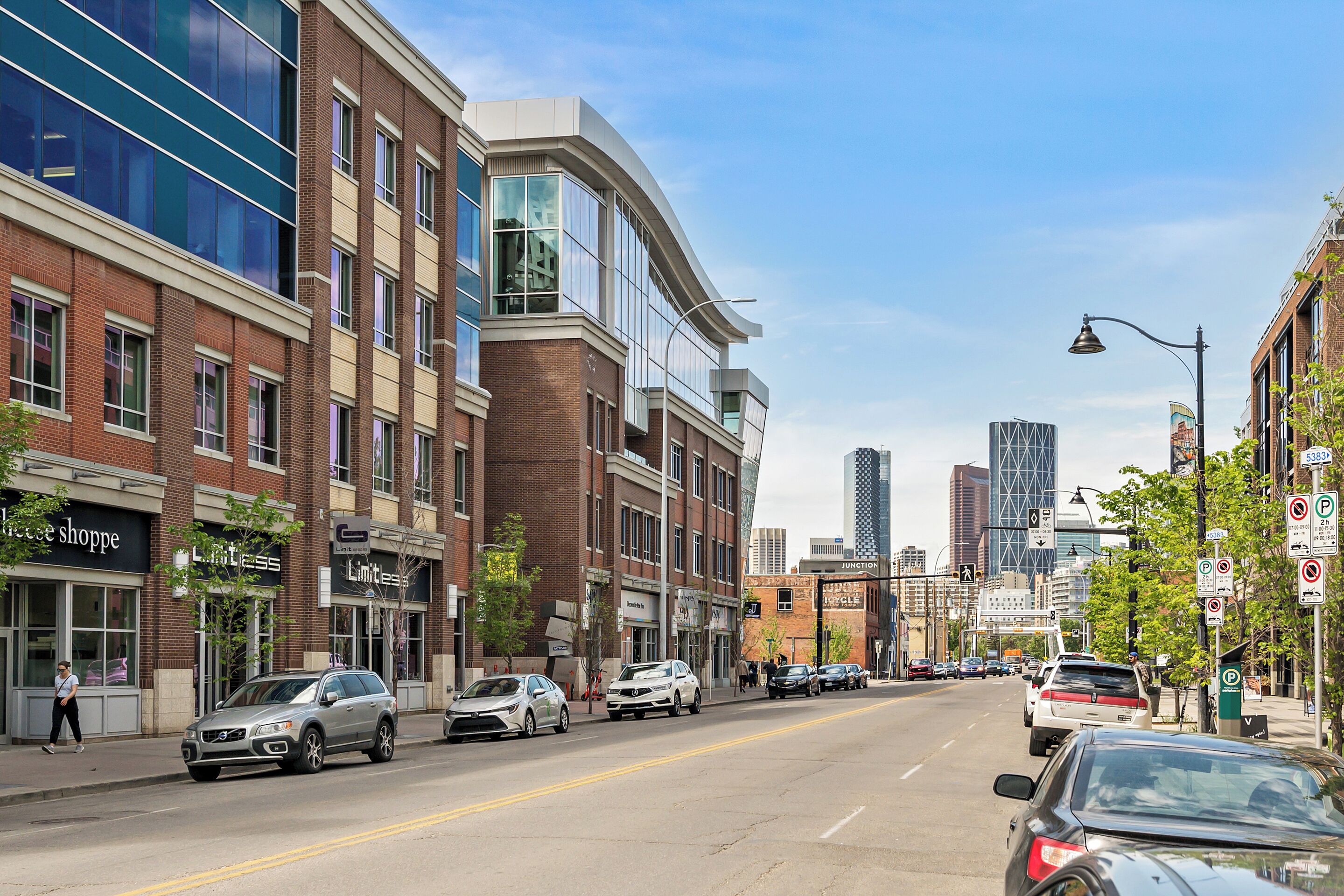 A street view with modern buildings, parked cars, and a clear sky.
