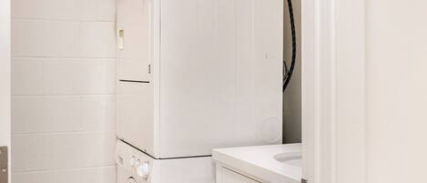 A laundry area with stacked washers and dryers, a sink, and a cabinet with gold handles.