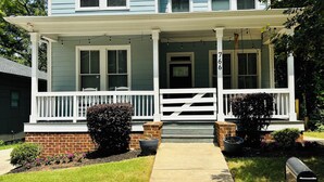 Une maison à deux étages avec un porche à l’avant, des fondations en briques et une boîte aux lettres.