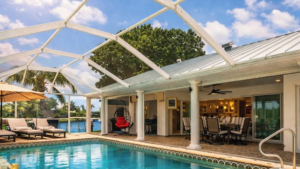 A pool area with a glass ceiling, lounge chairs, a red chair, and a dining area with tables and chairs. - La Dolce Vita: Your Waterfront Jackpot (North Fort Myers)