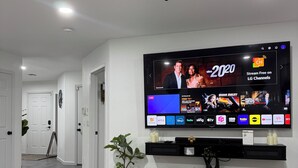 Un salon moderne doté d’un téléviseur à écran plat fixé au mur, d’un ventilateur de plafond et d’un coin repas avec une table et des chaises.