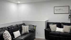 Un salon moderne avec deux canapés en cuir noir, un mur blanc à texture, et un plafond doté d’un éclairage encastré et d’une bouche d’aération.