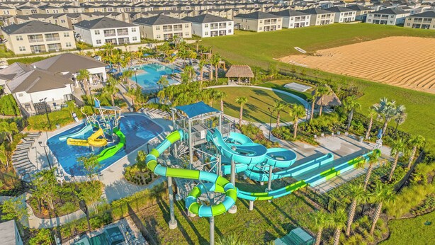 An aerial view of a resort with a large pool area, water slides, and a well-maintained lawn. - Charming 2-bedroom townhome in Kissimmee with WiFi, fitness room, AC (Kissimmee)