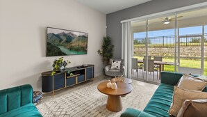 A modern living room with a teal sofa, a wooden coffee table, and a large flat-screen TV mounted on the wall. - Charming 2-bedroom townhome in Kissimmee with WiFi, fitness room, AC (Kissimmee)