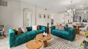 A modern living room with teal sofas, a wooden coffee table, and a dining area with a round table. - Charming 2-bedroom townhome in Kissimmee with WiFi, fitness room, AC (Kissimmee)