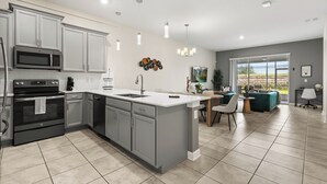 A modern kitchen with grey cabinets, a central island, and a dining area with a view. - Charming 2-bedroom townhome in Kissimmee with WiFi, fitness room, AC (Kissimmee)