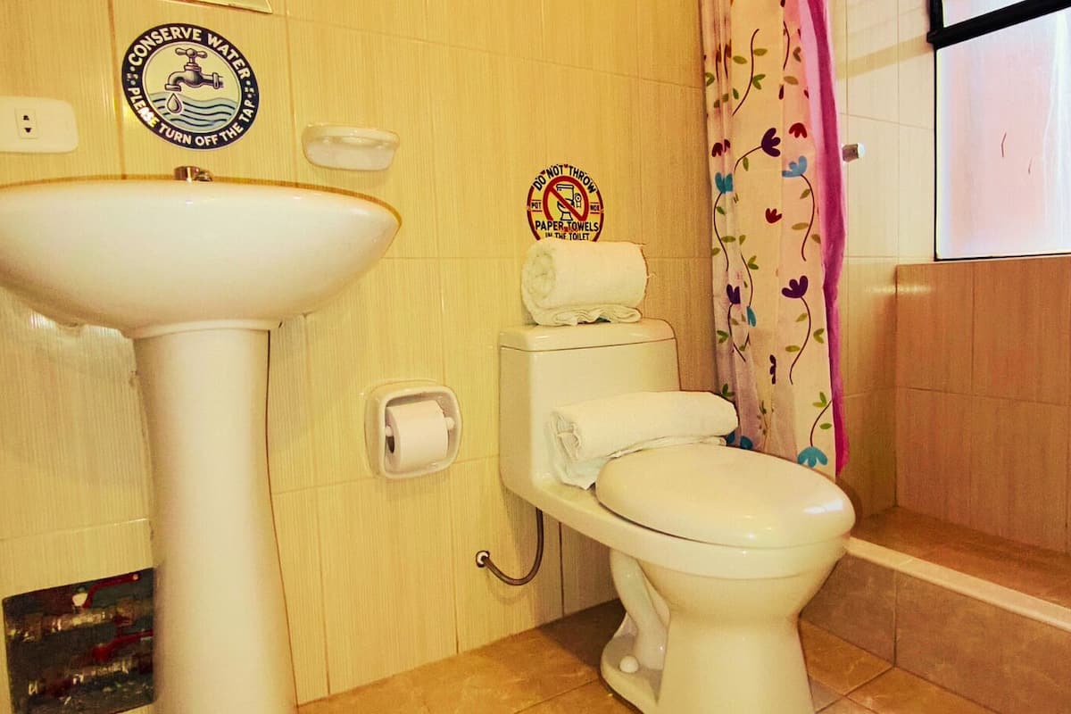 A bathroom with a sink, toilet, and a toilet paper holder. There are stickers on the wall, one of which says "Conserve Water - Please Turn Off The Tap".