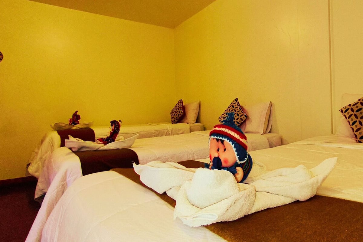 A hotel room with two beds, each with white linens and patterned pillows. A plush toy is placed on the bed in the foreground.