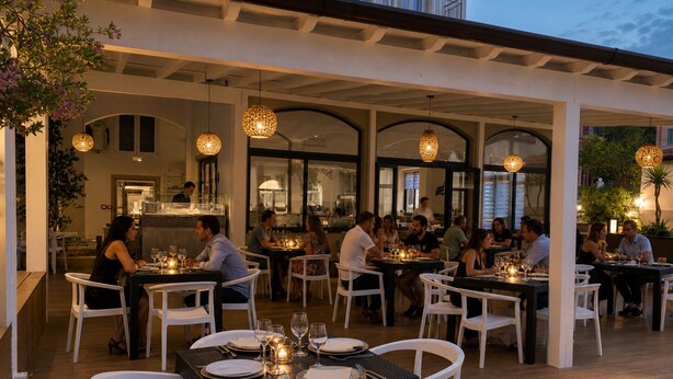 An outdoor dining area with tables and chairs, a covered section with a kitchen in the background, and hanging lights. - Primo Hotel (Marciana Marina)