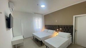 A hotel room with two single beds, a desk, a TV, and a door. - Primo Hotel (Marciana Marina)