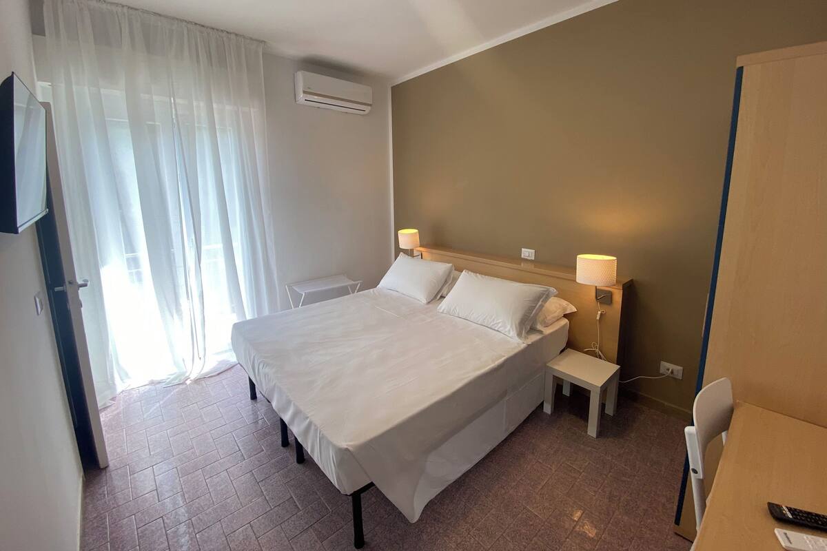 Habitación de hotel con cama, lámparas de noche, una mesita, aire acondicionado y televisor en la pared.