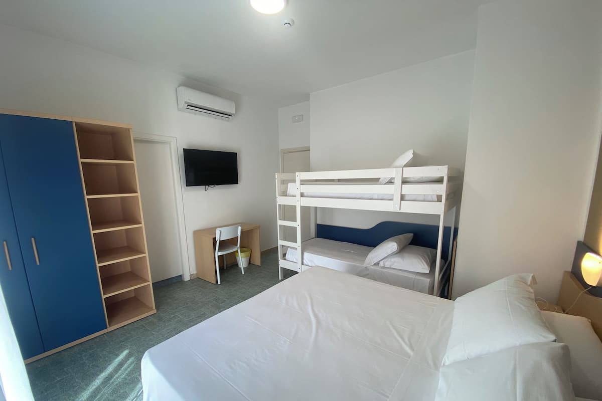 Habitación de hotel con camas literas, un escritorio con silla, armario y televisor de pantalla plana en la pared.