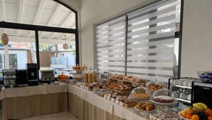 A buffet setup with various food items, a coffee station, and a view through large windows. - Primo Hotel (Marciana Marina)