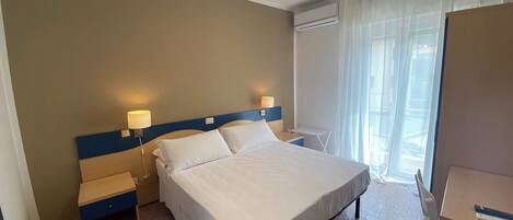 A hotel room with a large bed, bedside tables, a desk, and a window with curtains.