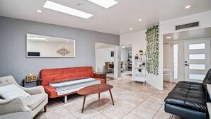 A modern living room with a red sofa, a white sofa, a coffee table, and a black leather chair. There is a white bookshelf with plants and a white door with frosted glass panels. - 3-bedroom house in beautiful Tucson with WiFi, AC (Tucson)
