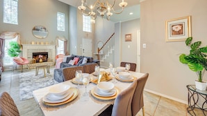A dining area with a table set for four, a chandelier, and a fireplace in the background.