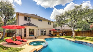 A backyard with a swimming pool, red lounge chairs, and a wooden deck.