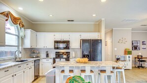 A modern kitchen with white cabinets, a central island with bar stools, stainless steel appliances, and a large window with curtains.