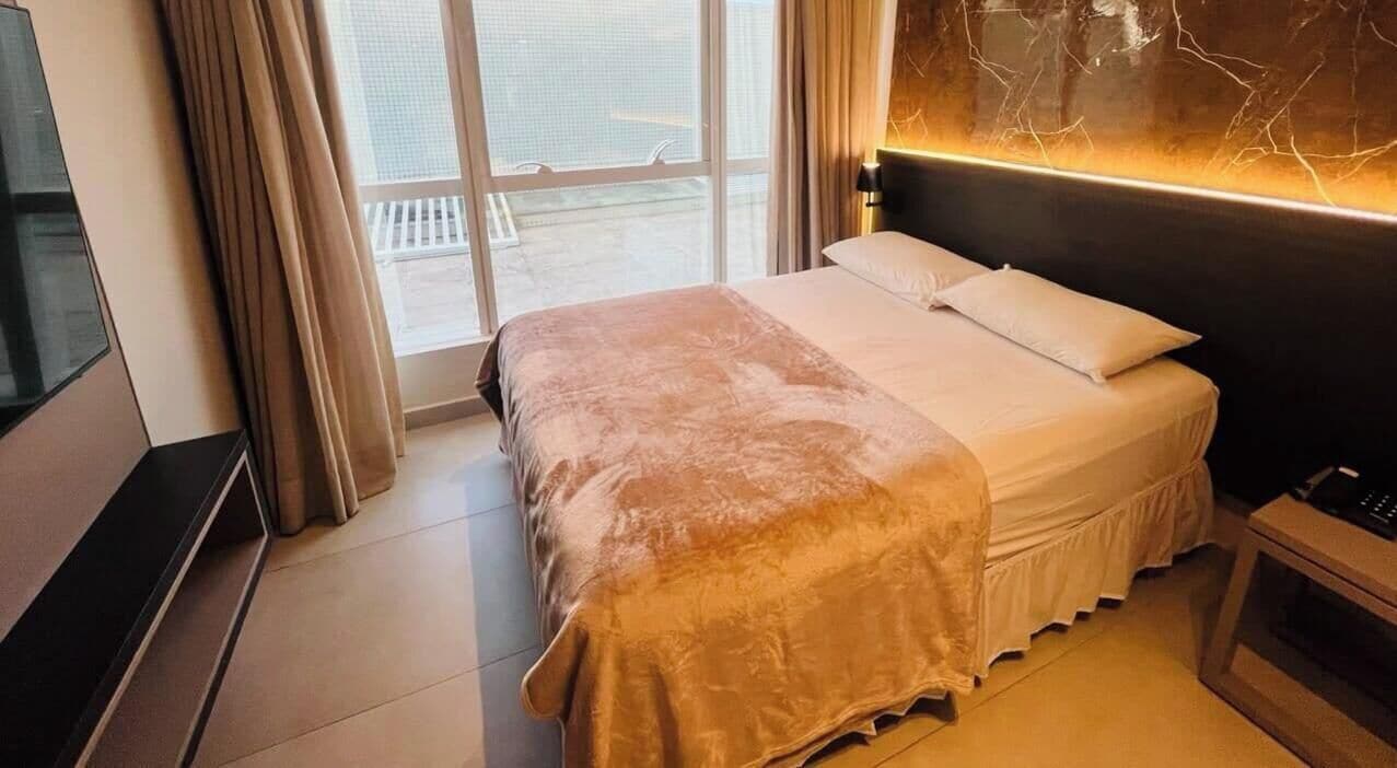 Una camera d'albergo con un letto, una televisione, una finestra con tende e una parete con una crepa.