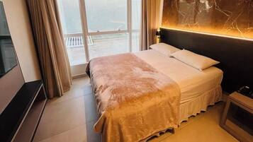 Una habitación de hotel con cama, televisión, ventana con cortinas y una grieta en la pared.