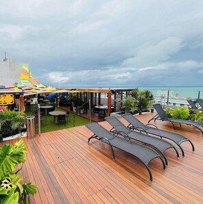 Une terrasse en bois avec des chaises longues, un espace salon couvert et une vue sur l’océan.