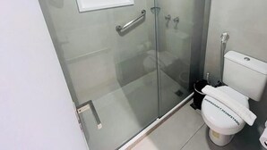 Une salle de bain moderne avec une douche à parois de verre, des toilettes blanches et une petite fenêtre située au-dessus des toilettes.