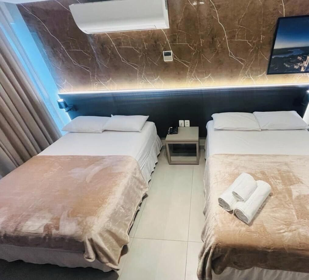A hotel room with two beds, a nightstand, a wall-mounted air conditioner, and a small picture frame.