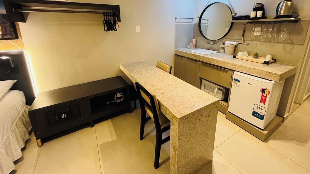 A compact hotel room with a kitchenette, a bed with a headboard, and a small seating area.