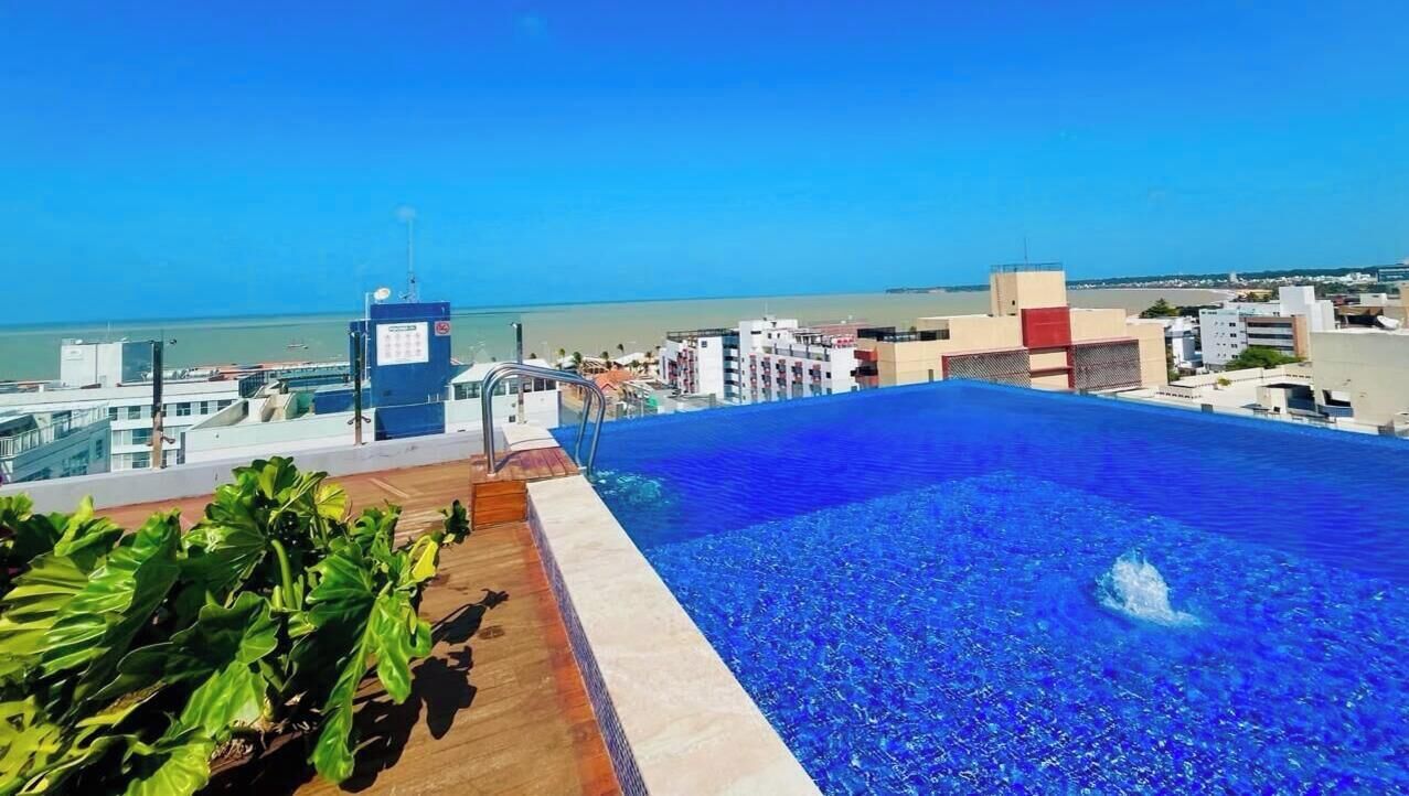 A rooftop infinity pool with a clear view of the ocean and cityscape.