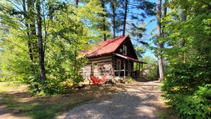Eine rustikale Holzhütte mit Schotterzufahrt, umgeben von dichtem Baumbestand.