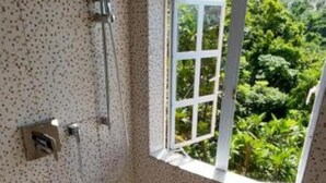 Un petit espace de douche fermé, doté d’une fenêtre, de murs carrelés et d’un pommeau de douche.