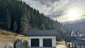 A garage with a dark roof and white walls, surrounded by a paved driveway and a concrete wall. - Selway Chalet (Kooskia)