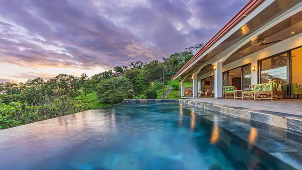 Une maison moderne dotée d’une piscine, de grandes fenêtres et offrant une vue sur la verdure environnante.