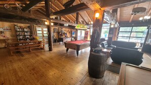 A wooden-floored room with a pool table, a bar area, and a billiards table. - Jack Pine Cabin at Pine Ridge Park (Pembroke)