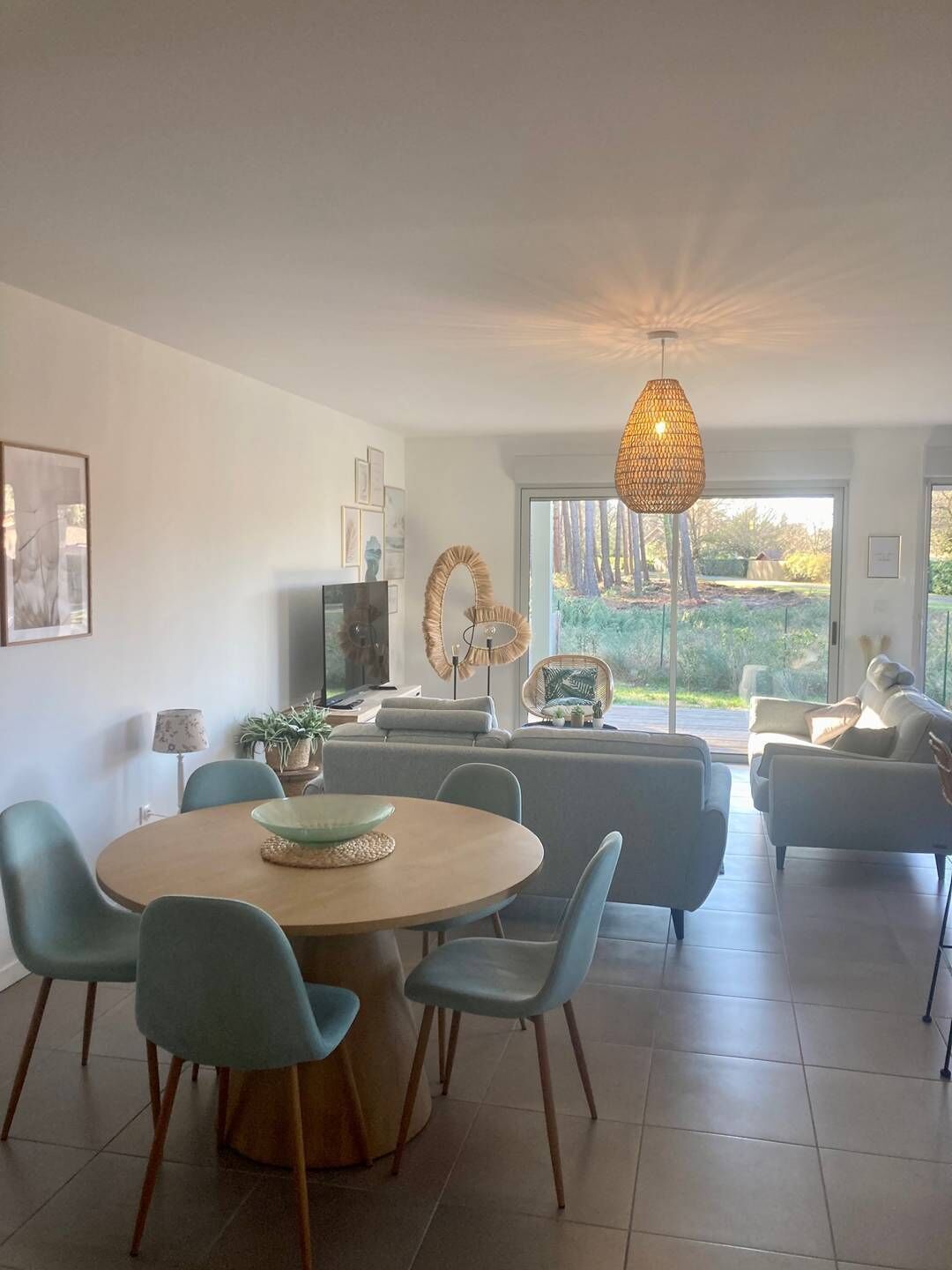 Un salon moderne avec une table à manger ronde, des chaises bleu clair, un canapé et une grande fenêtre donnant sur un paysage verdoyant.