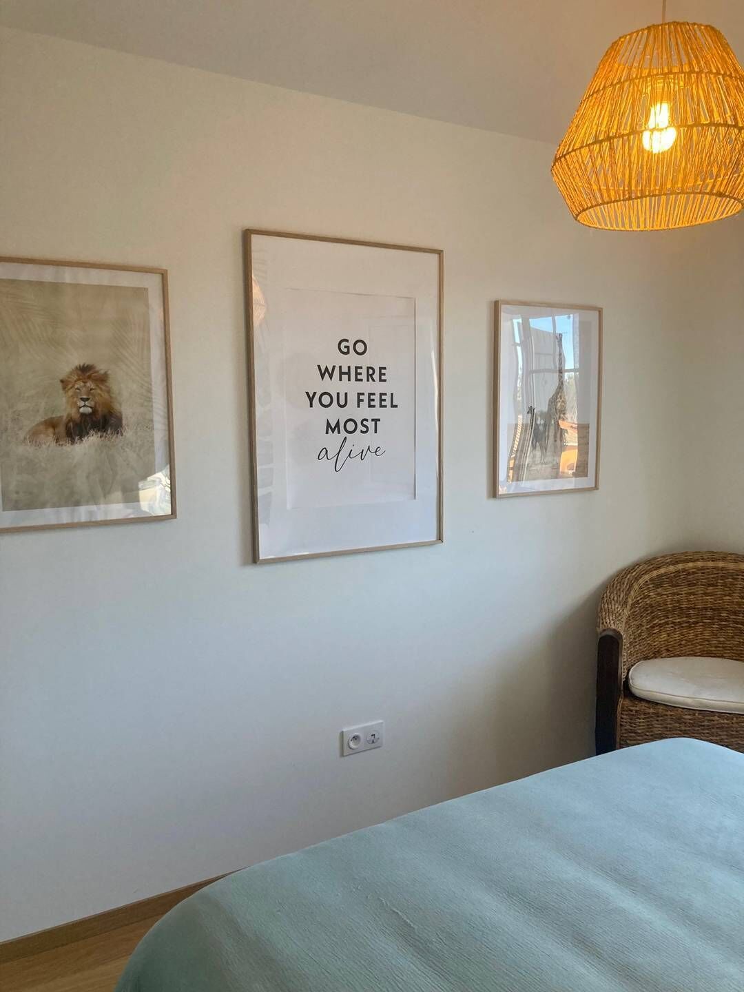 Een slaapkamer met een bed, een rieten stoel en drie ingelijste kunstwerken aan de muur.