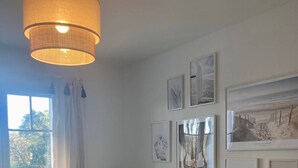 A bedroom with a bed, a window with curtains, a wall-mounted lamp, and several framed pictures. - Les Fougères - Moliets (MOLIETS ET MAA)