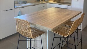 A modern kitchen with a large island, two bar stools, pendant lighting, and a window providing natural light. - Les Fougères - Moliets (MOLIETS ET MAA)