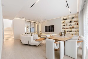Una sala de estar moderna con un sofá, una mesa de comedor, sillas, un televisor y una estantería.