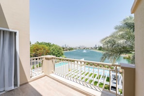 A balcony with a view of a swimming pool, palm trees, and a distant cityscape. - Luxury Villa with Pool and Garden 4BR The Springs (Dubai)