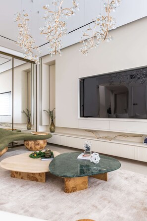 Una sala de estar moderna con un televisor de pantalla plana grande, un sofá verde y una mesa de centro redonda con tapa de vidrio.