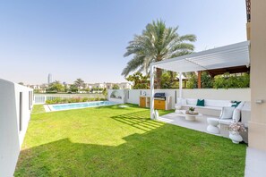 A modern outdoor living area with a pool, seating, and a view of the city skyline. - Luxury Villa with Pool and Garden 4BR The Springs (Dubai)