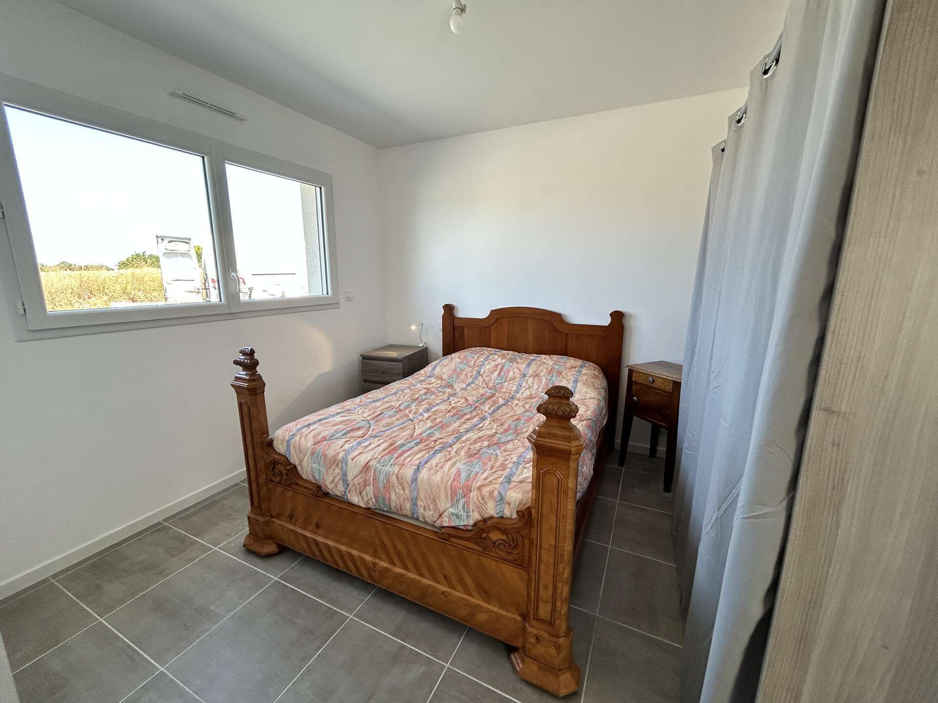 A bedroom with a wooden bed, a small bedside table, a nightstand, and a window with a view of the outside.
