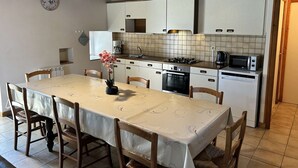A compact kitchen with a dining table, chairs, and basic appliances. - Family house with terrace in Fréhel | 8 guests | Ref 301 (FREHEL)