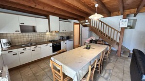 A kitchen with wooden beams, a dining table with chairs, a microwave, a stove, and a refrigerator. - Family house with terrace in Fréhel | 8 guests | Ref 301 (FREHEL)