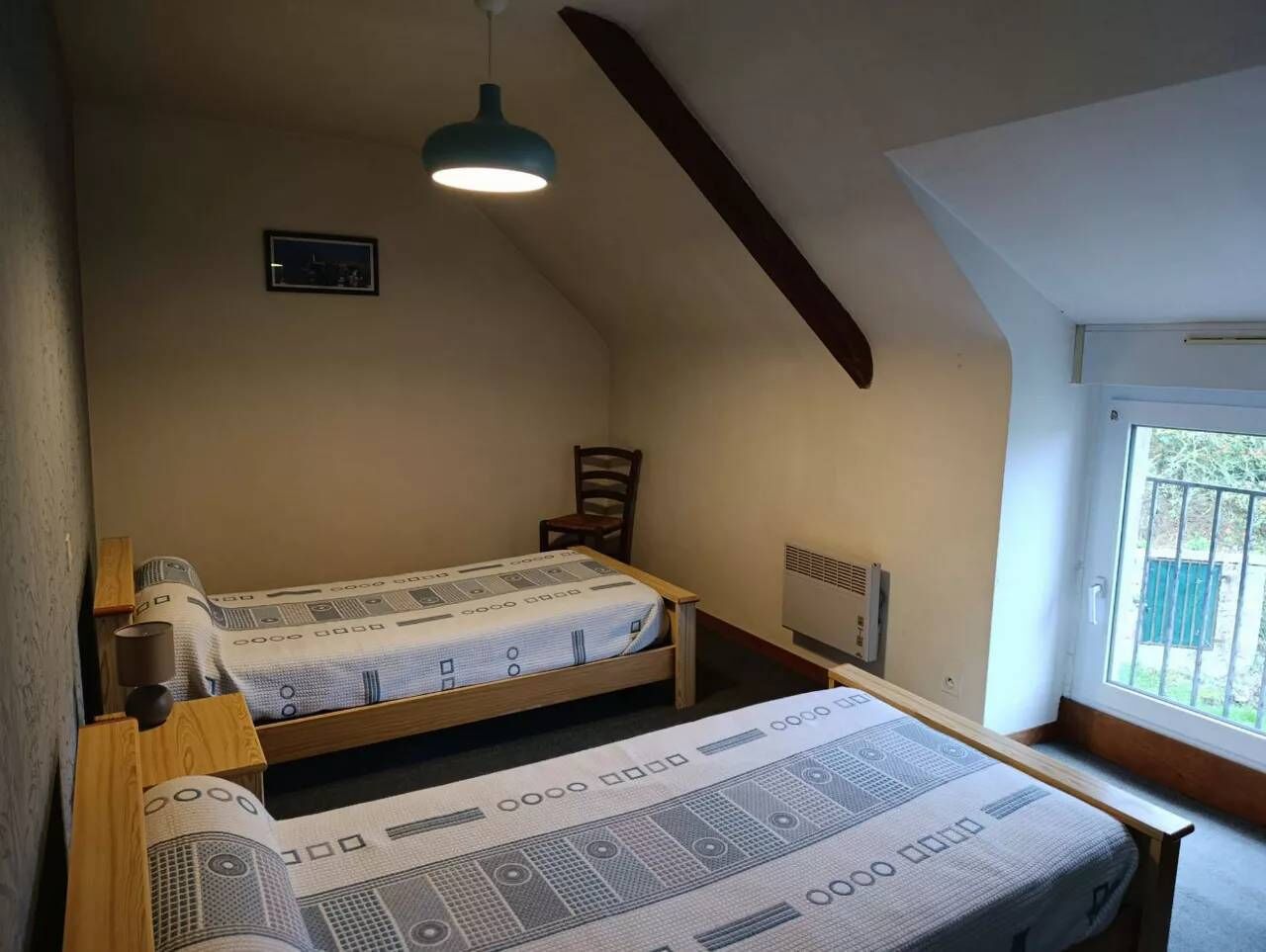 Une petite chambre agréable, dotée de deux lits simples, d’une tête de lit en bois, d’un ventilateur de plafond et d’une fenêtre laissant entrer la lumière naturelle.