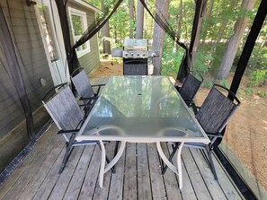 Une table avec un plateau en verre, quatre chaises, un barbecue et une terrasse en bois.