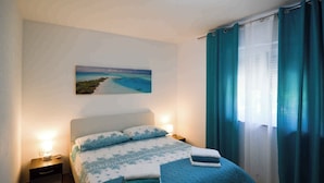 Ein ordentlich bezogenes Bett mit einer blauen und weißen Bettdecke, zwei Kissen und zwei gefaltete Handtücher auf der Seite.