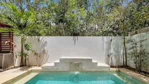 A swimming pool with a waterfall feature, surrounded by lush greenery and a white wall. - Senderos De Ciudad Mayakoba (Playa del Carmen)